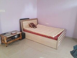 Ein kleines Zimmer mit einem Einzelbett, einem Holz-Kopfteil, einem Nachttisch mit Radio und einem roten Bettbezug.