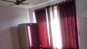 A room with a ceiling fan, a wardrobe, a bed, and a window with red curtains.
