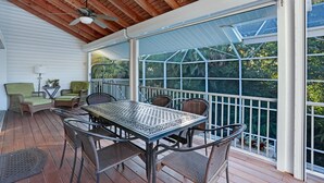 Un patio techado con una mesa y sillas, un ventilador de techo y vistas al exterior a través de un cerramiento de vidrio.