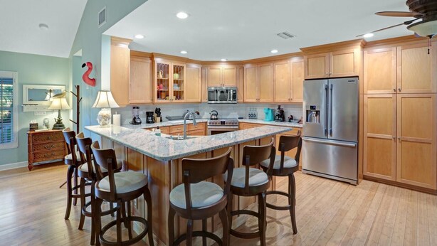 Una cocina moderna con una isla grande, armarios de madera, electrodomésticos de acero inoxidable y un comedor con taburetes de bar.
