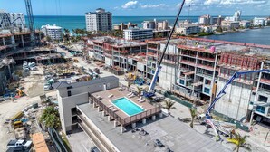 A hotel with a rooftop pool, construction cranes, and a view of the ocean. - Cozy Condo With Pool Steps From Vanderbilt Beach (Naples)