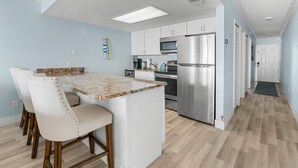 A modern kitchen with white cabinets, stainless steel appliances, and a marble countertop. - Cozy Condo With Pool Steps From Vanderbilt Beach (Naples)