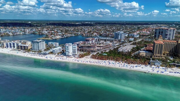 An aerial view of a coastal city with a beachfront, high-rise hotels, and a marina. - Cozy Condo With Pool Steps From Vanderbilt Beach (Naples)
