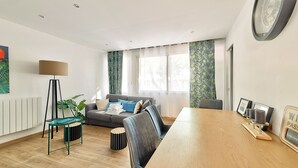 Een moderne woonkamer met een houten eettafel, een grijze bank, een vloerlamp en een groot raam met behang.