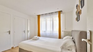 Een slaapkamer met een bed, een radiator, een raam met gordijnen en een muur met ingelijste foto's.