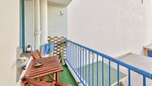 Een balkon met een houten tafel en stoelen, een blauwe balustrade en een klein tuintje met planten in potten.