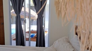 A bedroom with a bed, curtains, and a view of an outdoor pool area.