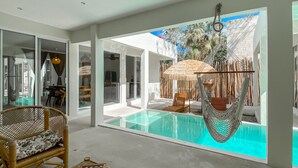 A modern pool area with a hammock, lounge chairs, and a view of a tropical garden.
