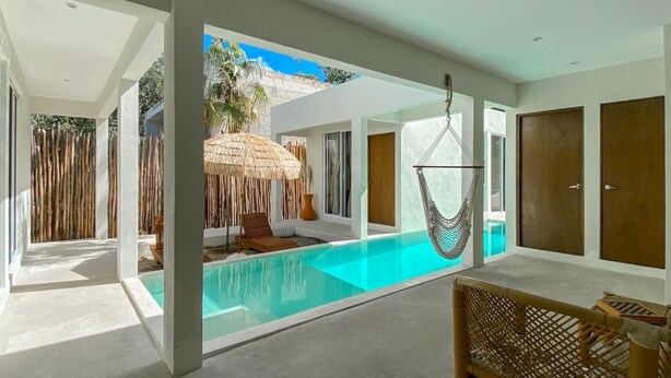 A modern pool area with a clear pool, a hammock, and a thatched umbrella.