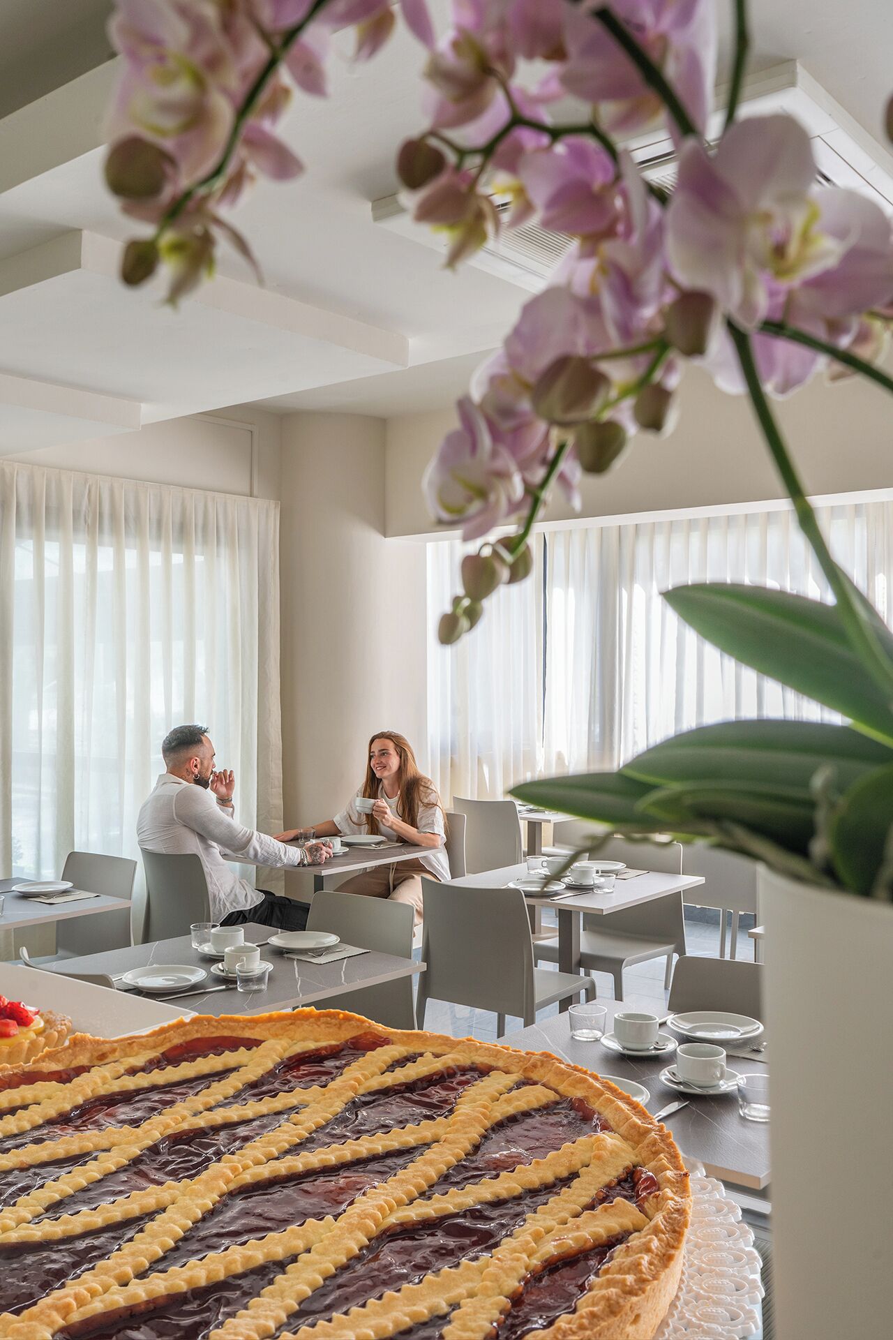 Uma sala de jantar com uma torta grande na mesa, cortinas brancas e um vaso de planta.
