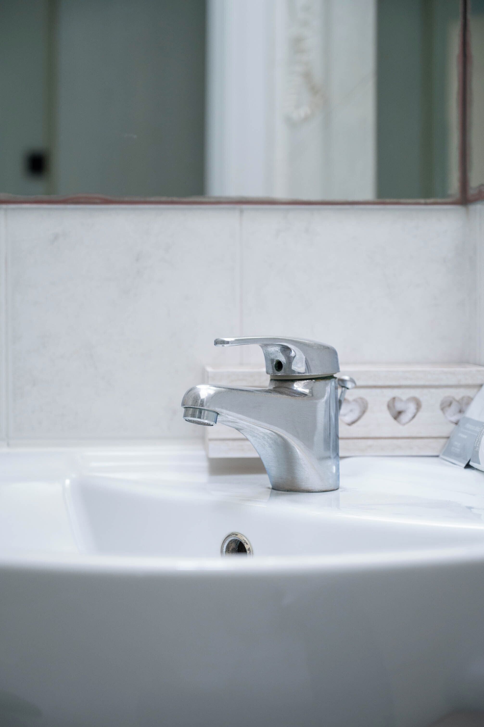 Une salle de bain avec un lavabo blanc, un robinet chromé et un miroir agrémenté d’un pare-éclaboussures en carreaux à motifs de cœur.