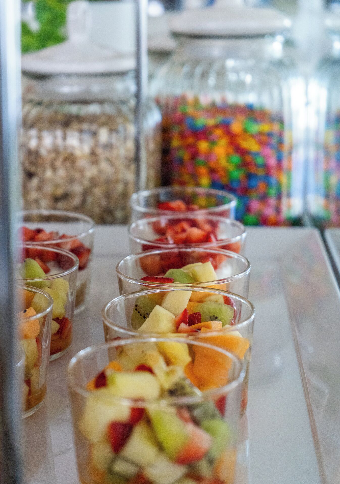 A display of fruit cups in clear glasses, with a blurred background of jars and containers.