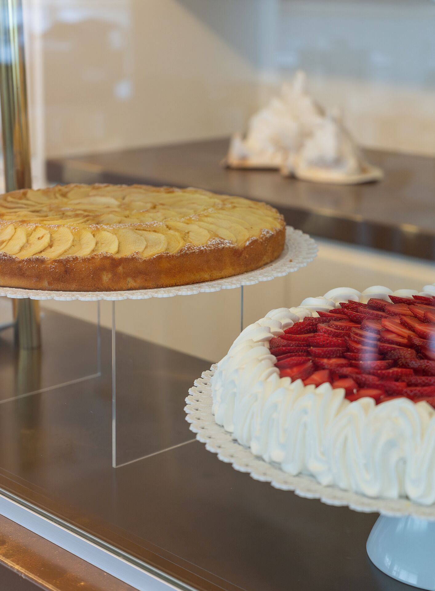 A display case with two cakes: one with apple slices and another with strawberries.