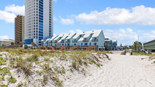 Un hotel frente a la playa con diseño moderno, que destaca por una torre imponente y varias edificaciones conectadas con balcones.