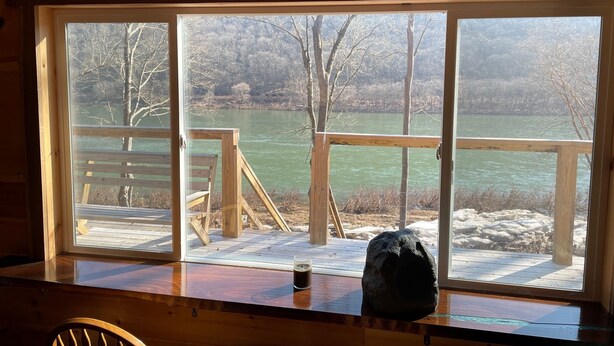 Eine Holzhütte mit einem großen Fenster mit Blick auf Fluss und Wald.