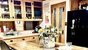 A wooden kitchen with a central island, chairs, and a refrigerator. - Rural western cabin- HOT TUB-POOL just 5 mins from exciting Stephenville! (Stephenville)