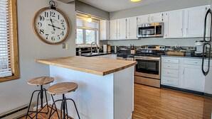 Cucina con mobili bianchi, isola in legno con sgabelli, orologio d'epoca e frigorifero in acciaio inossidabile.