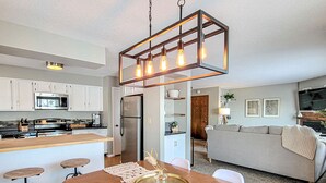 Una cucina moderna con mobili bianchi, un'isola in legno, sgabelli da bar, un'isola centrale con piano in vetro e un lampadario a sospensione.