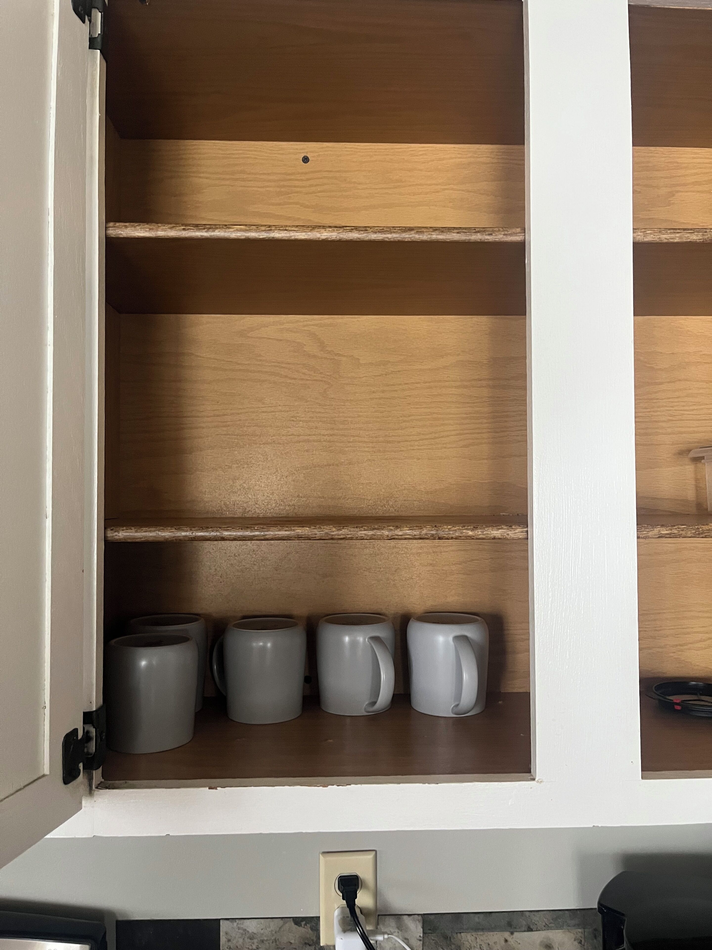 A kitchen cabinet with three grey mugs on the shelf.