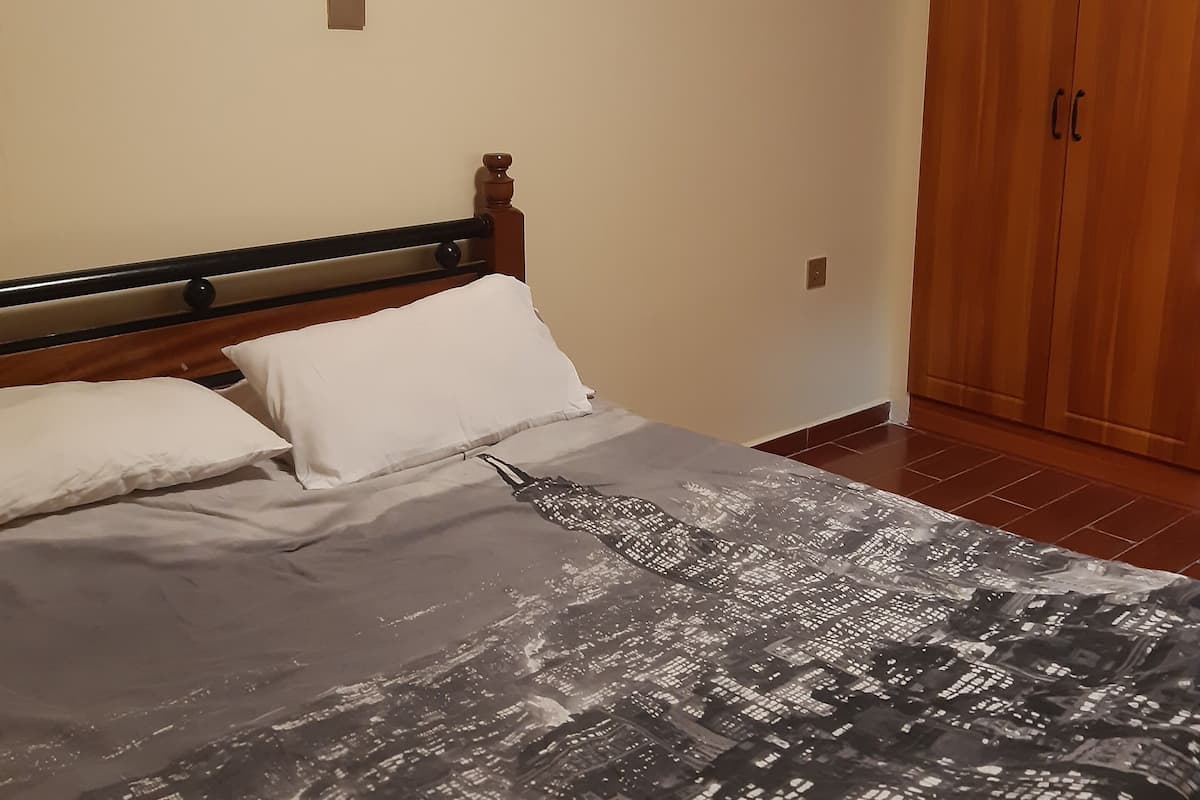 A bedroom with a bed, wooden wardrobe, and a cityscape bedspread.