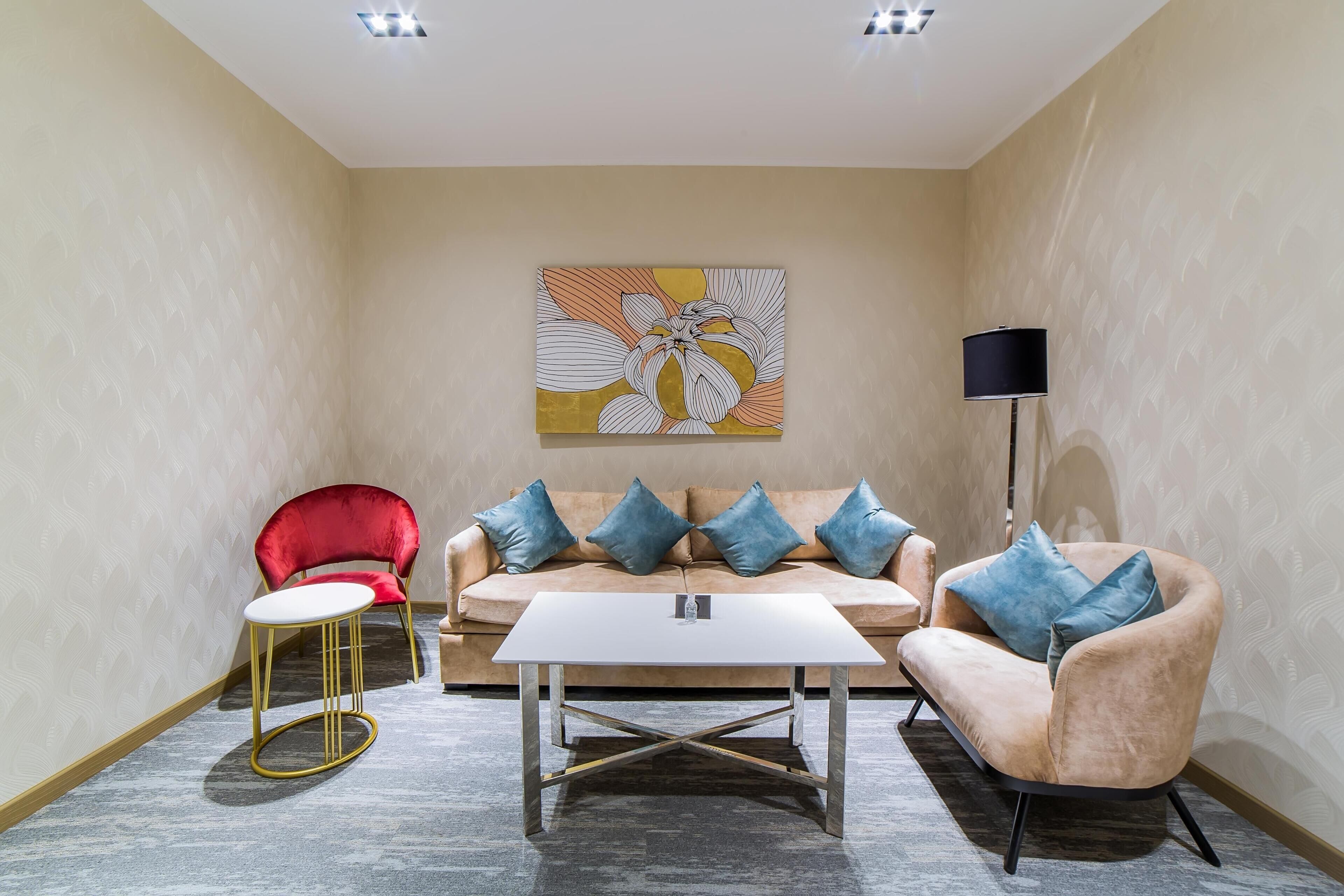 Une pièce avec un canapé beige, deux fauteuils, une petite table et un lampadaire.