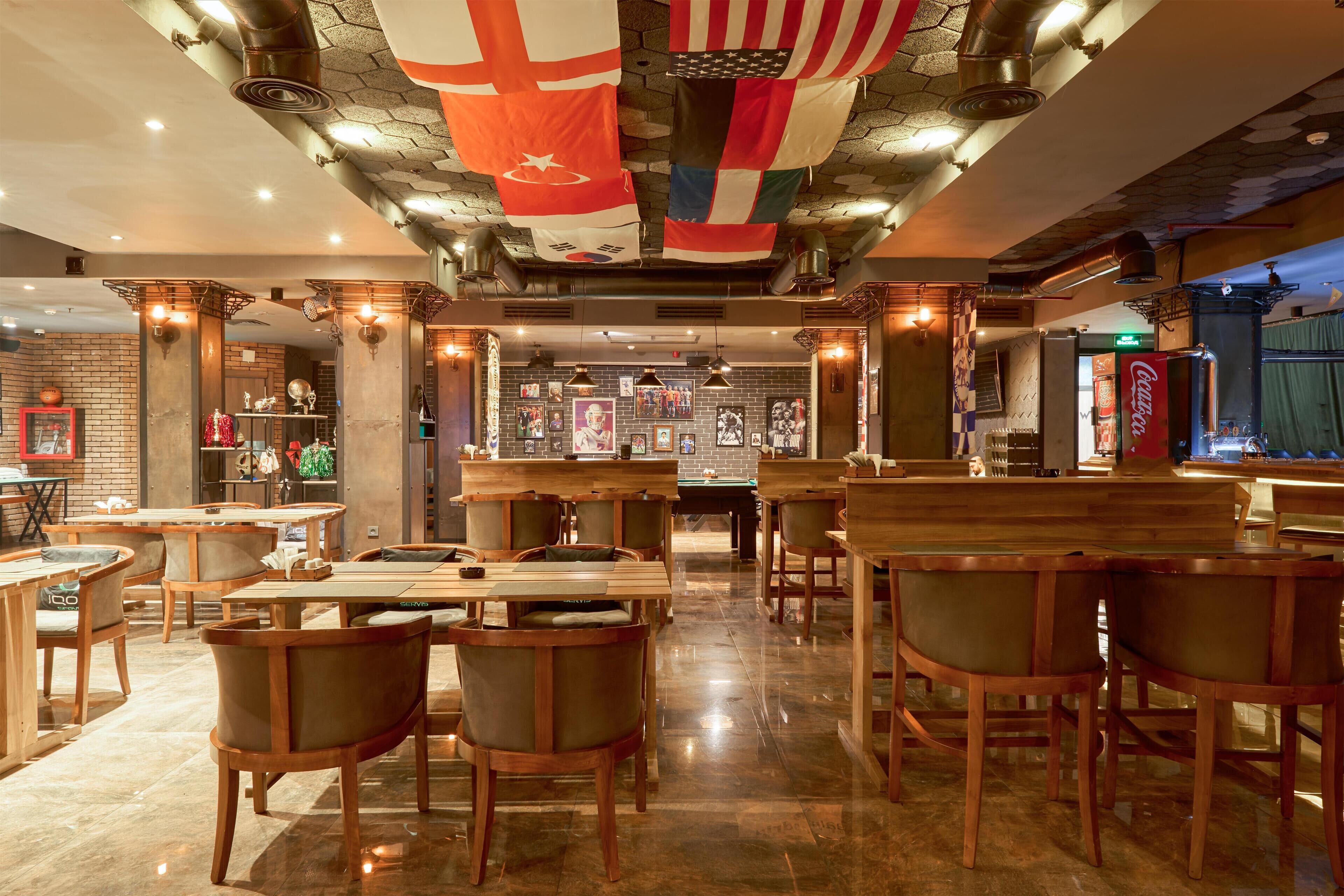 Un restaurant avec des tables et des chaises en bois, un coin bar et divers drapeaux suspendus au plafond.