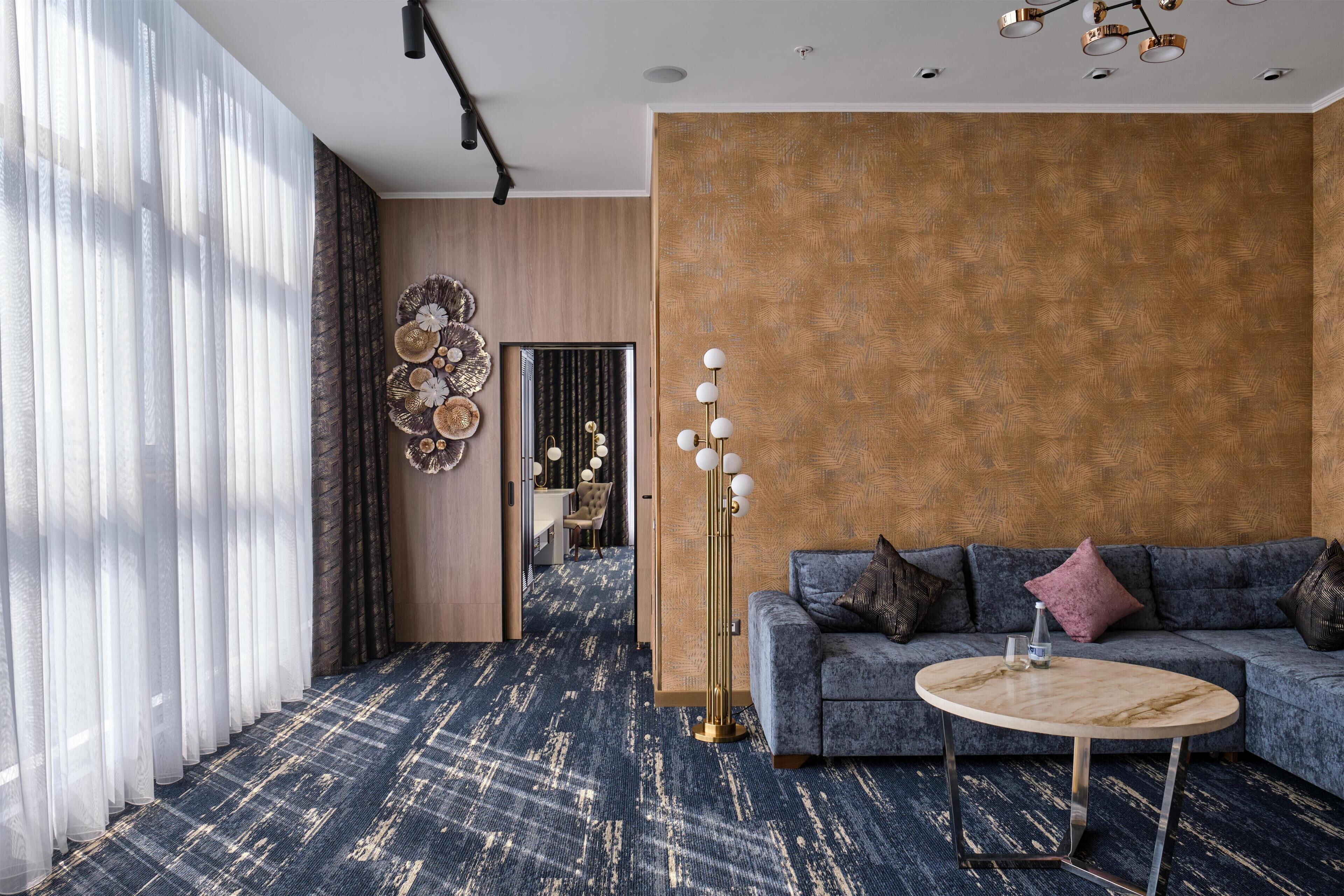 Una sala de estar moderna con alfombra azul, una mesa redonda de centro, un sofá gris con cojines y un adorno en la pared.