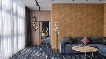 Una sala de estar moderna con alfombra azul, una mesa redonda de centro, un sofá gris con cojines y un adorno en la pared.