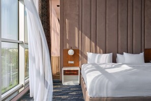 A modern hotel room with a large bed, a nightstand, a wooden headboard, and a view through a large window. - Panarams Tashkent Hotel, A member of Radisson Individuals (Tashkent)
