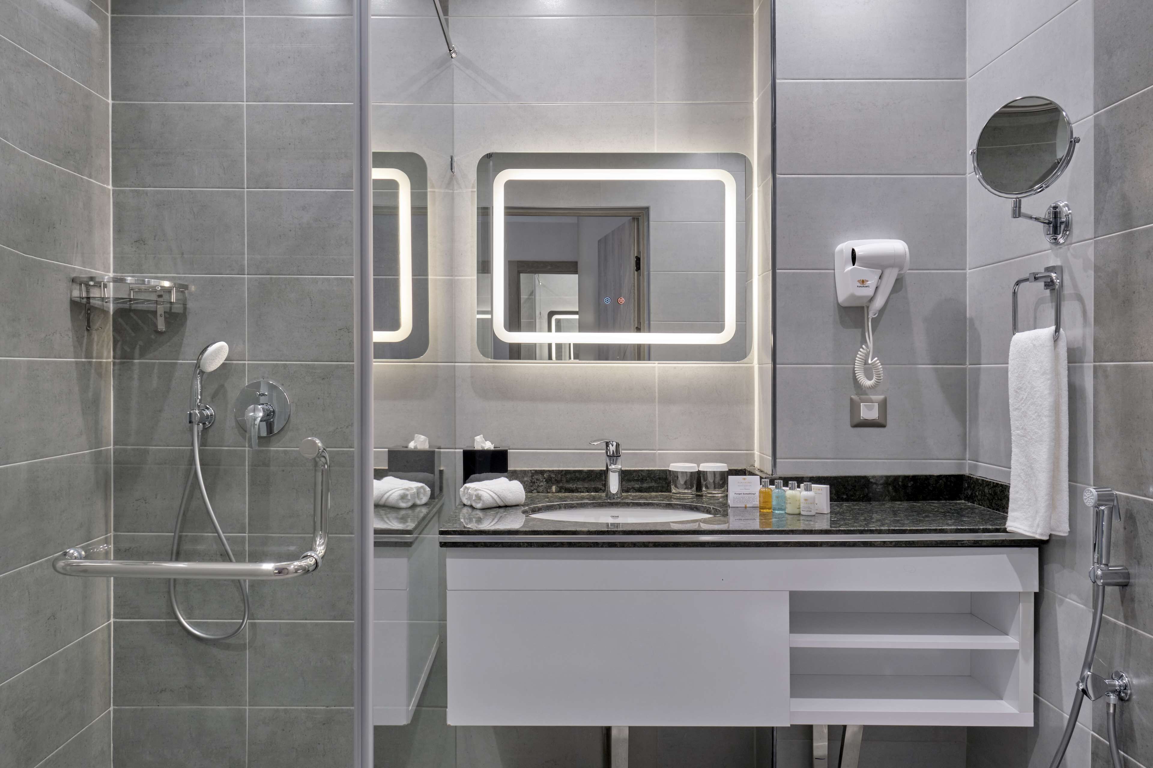 Casa de banho moderna com chuveiro de vidro, toucador com lavatório e secador de cabelo fixado na parede.