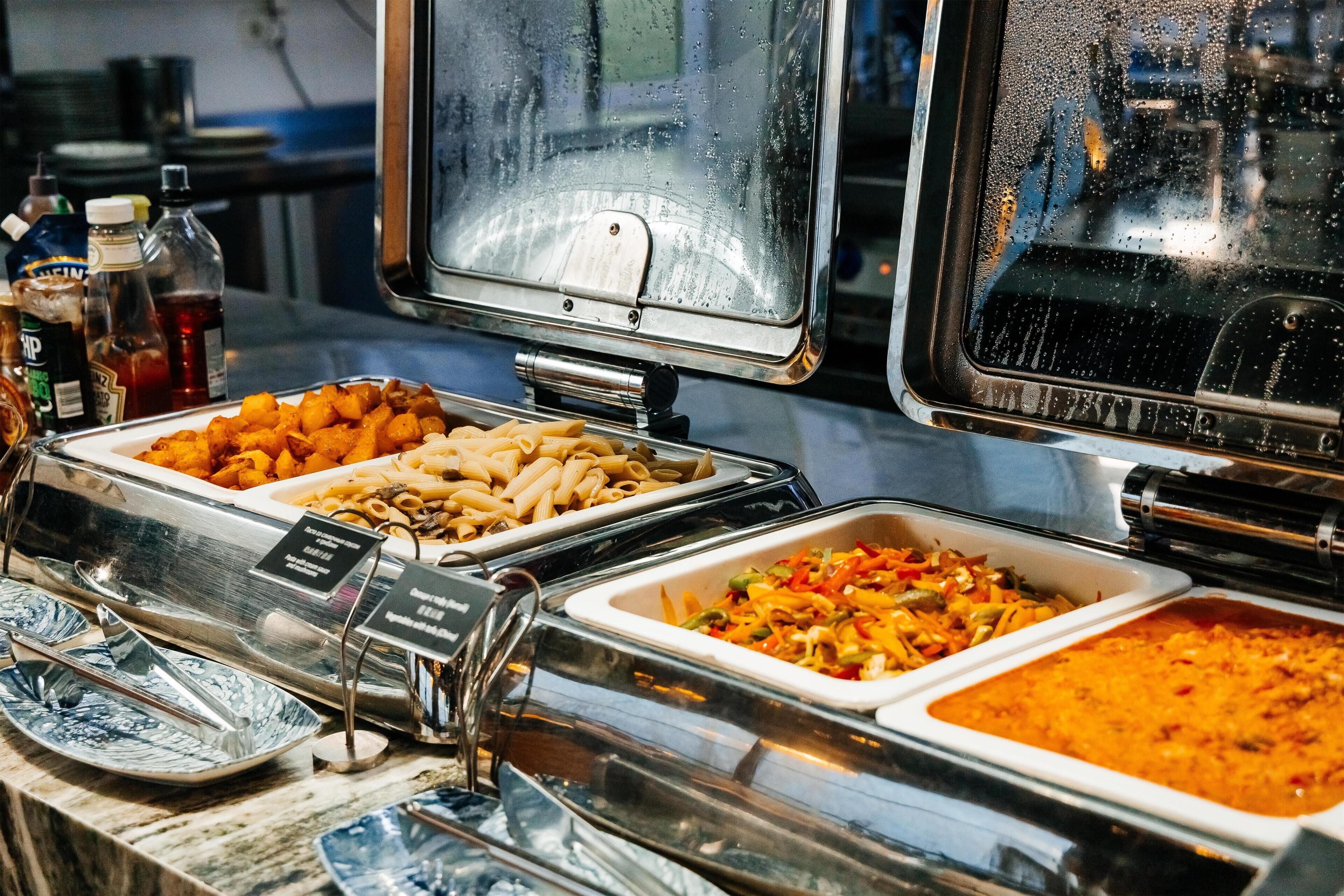 Buffet com diversas opções de comida, incluindo massa, legumes e uma salada de massa.