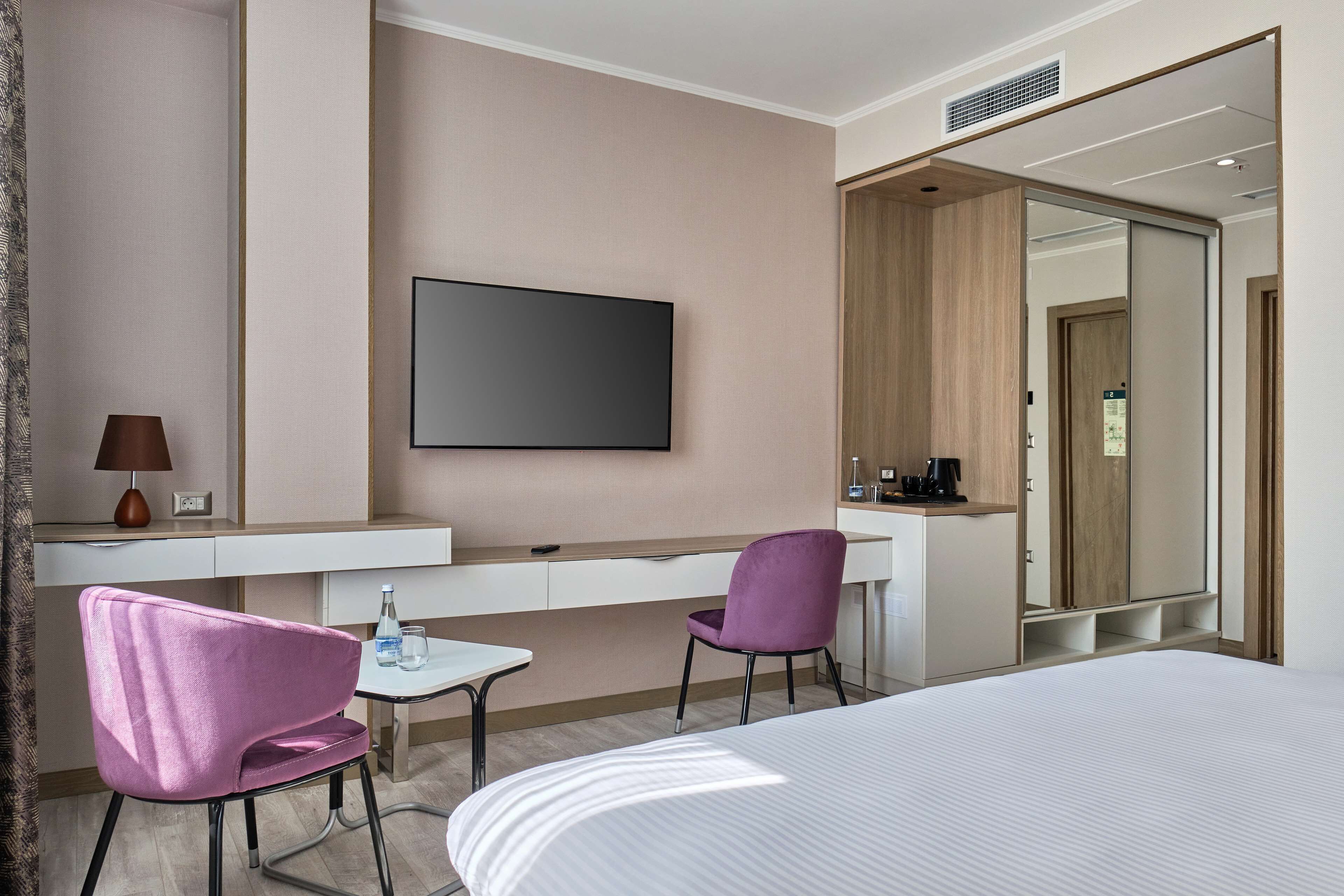 Une chambre d’hôtel équipée d’un lit, d’un bureau, d’une chaise, d’une télévision et d’un miroir.