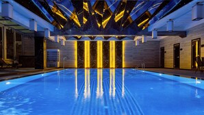 A modern indoor swimming pool with a reflective surface, geometric ceiling design, and ambient lighting. - Panarams Tashkent Hotel, A member of Radisson Individuals (Tashkent)