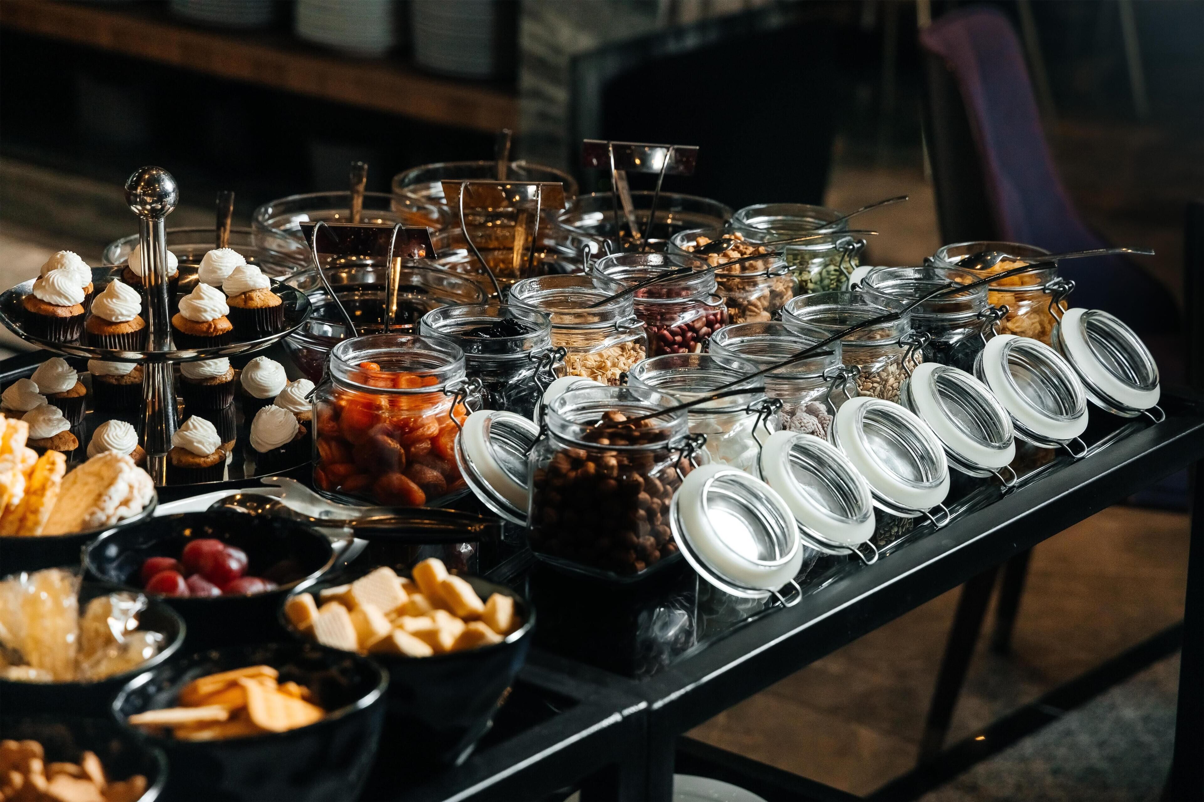 Monipuolinen buffet, jossa on tarjolla erilaisia ruokia ja ruokailuvälineitä.