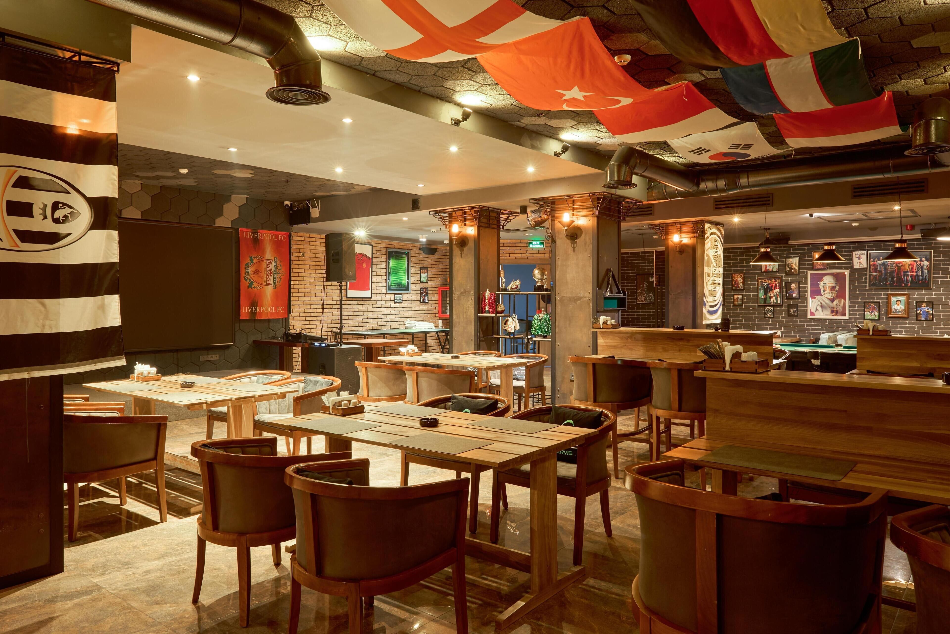 A restaurant with wooden tables and chairs, a bar area, and various flags hanging from the ceiling.