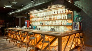 A bar area with a long counter, multiple stools, and shelves stocked with bottles. - Panarams Tashkent Hotel, A member of Radisson Individuals (Tashkent)