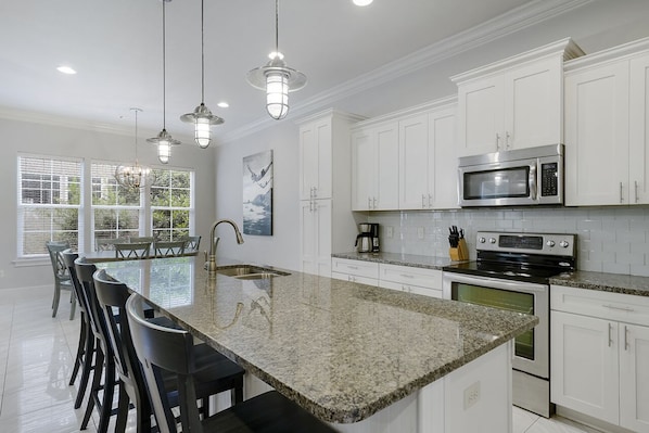 A modern kitchen with white cabinets, a granite countertop, stainless steel appliances, and pendant lighting.