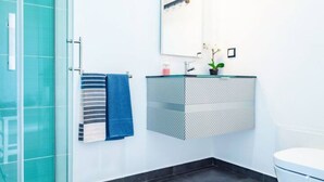A modern bathroom with a glass shower enclosure, a white toilet, and a floating sink with a potted orchid. - Infinito Azul II (Caniço)