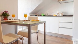 A modern kitchen with white cabinets, a stainless steel range hood, and a dining area with a table and chairs. - Infinito Azul II (Caniço)