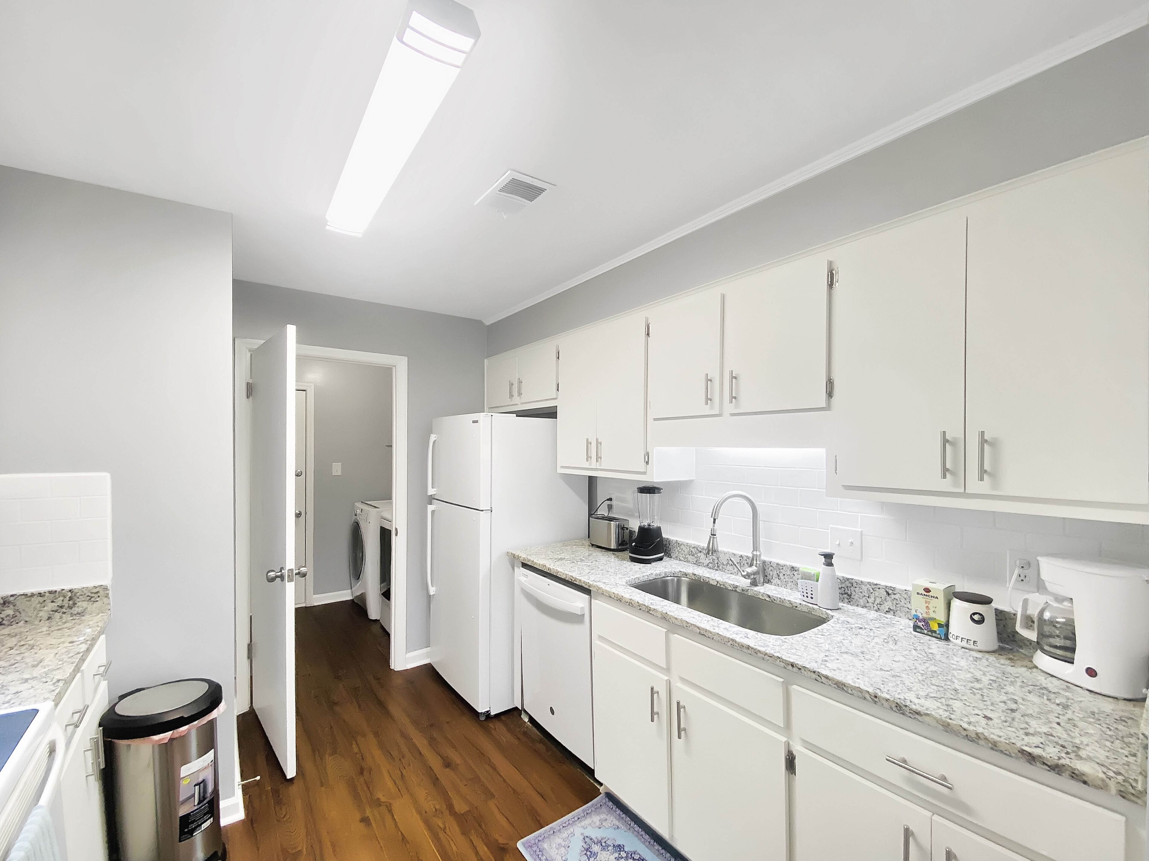 A modern kitchen with white cabinets, a stainless steel sink, and a built-in dishwasher.