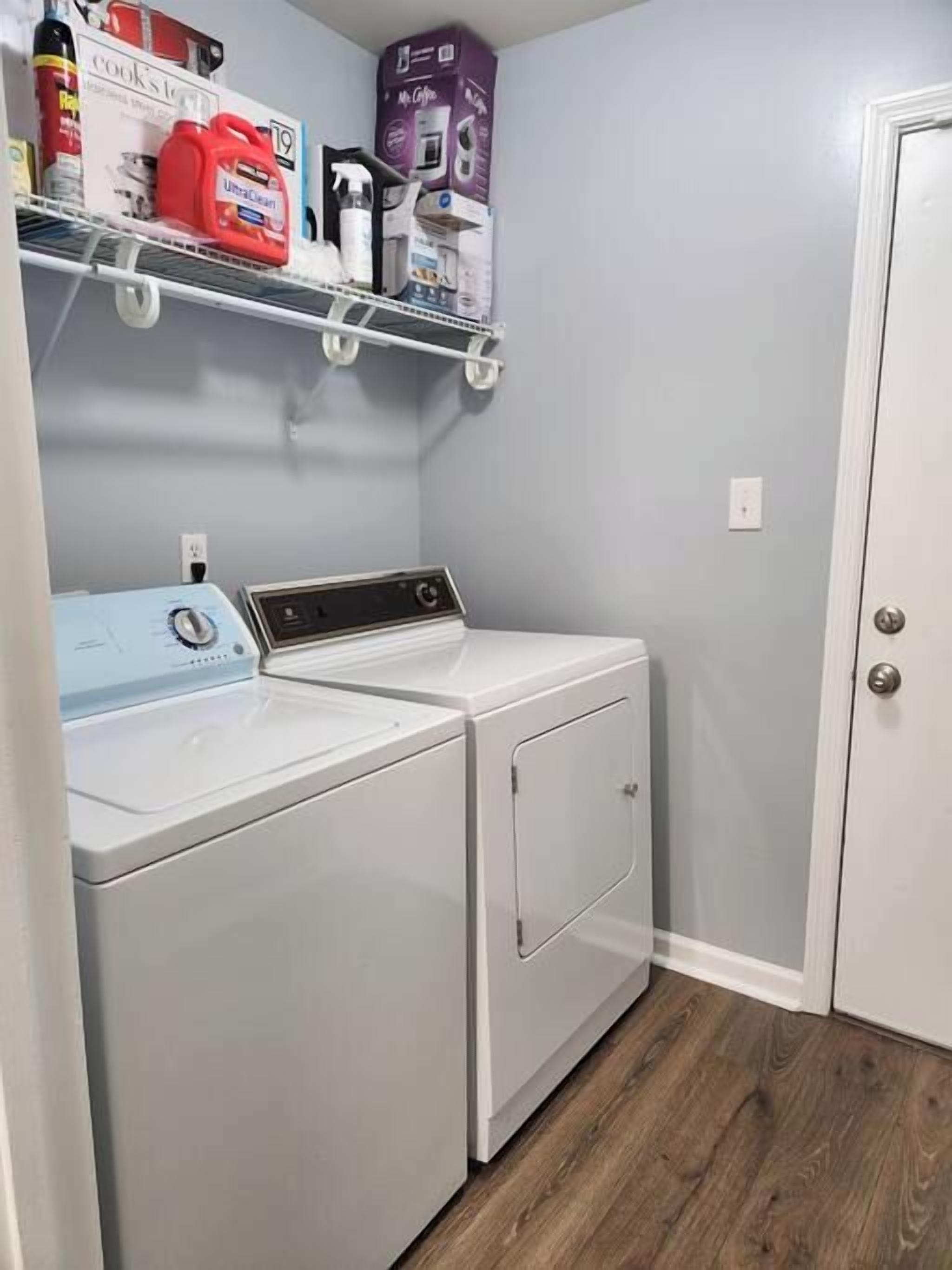 A laundry room with a washing machine and dryer, a shelf with cleaning supplies, and a door to the right.