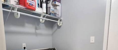 A laundry room with a washing machine and dryer, a shelf with cleaning supplies, and a door to the right.