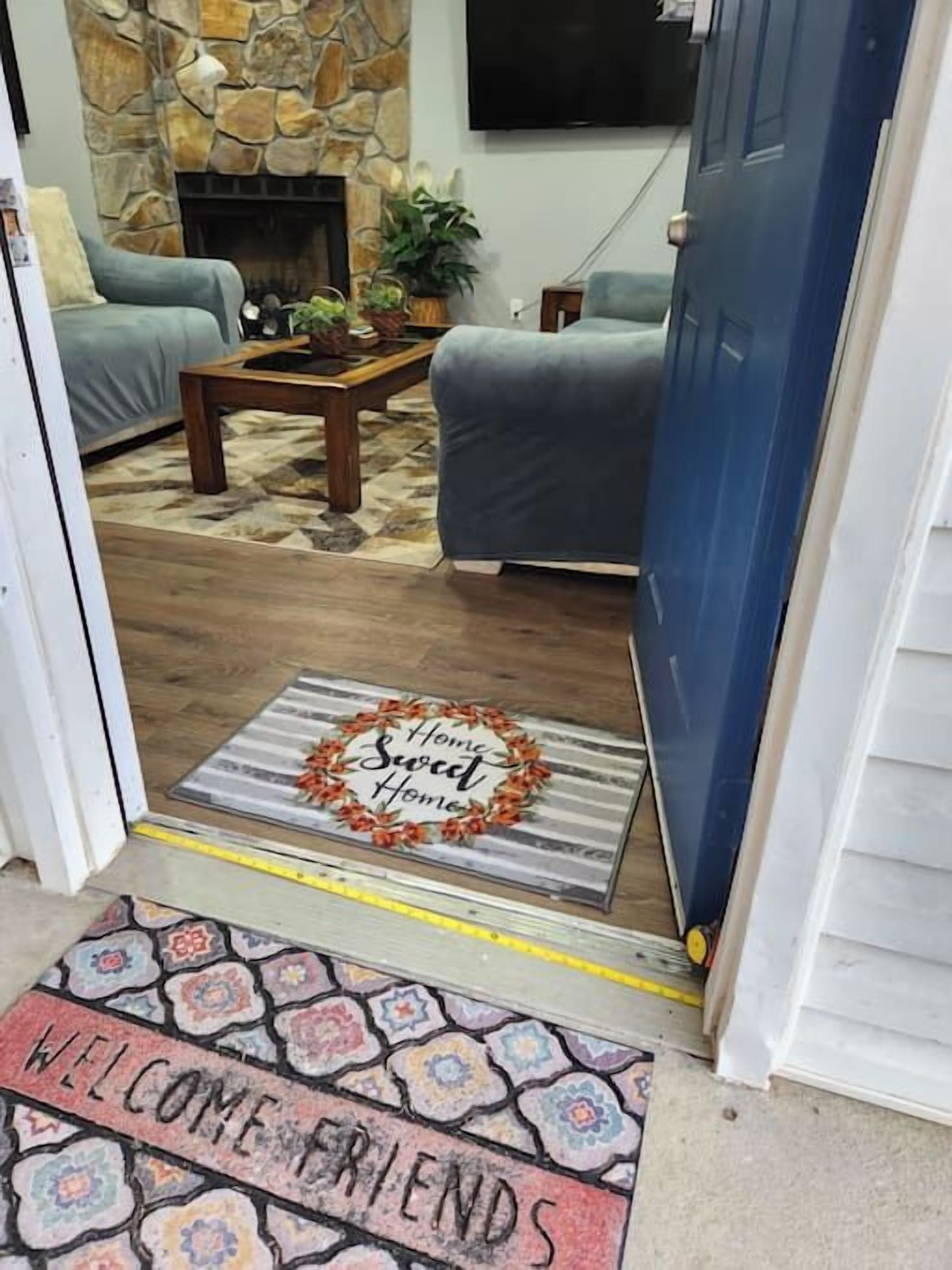 A living room with a stone fireplace, a blue door, and a welcome mat.