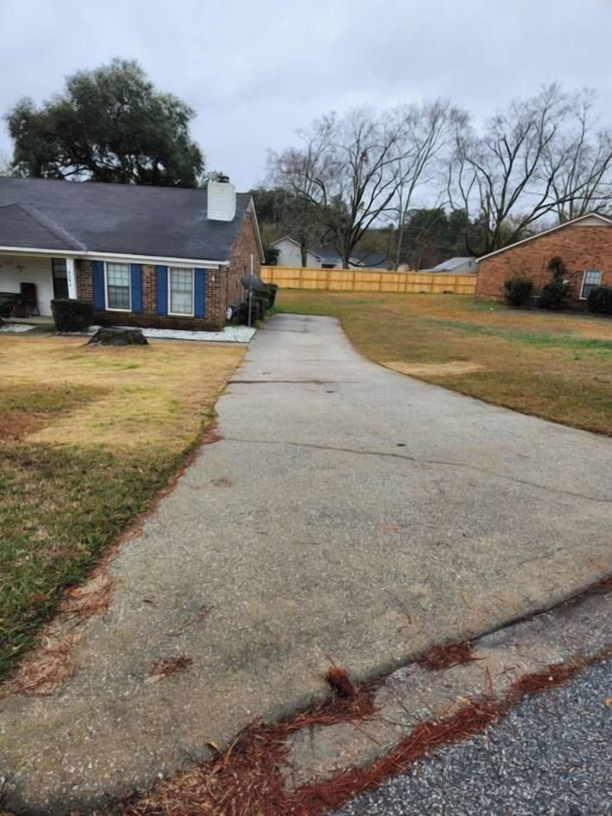 A residential driveway leading to a house with a brick facade and a dark roof.