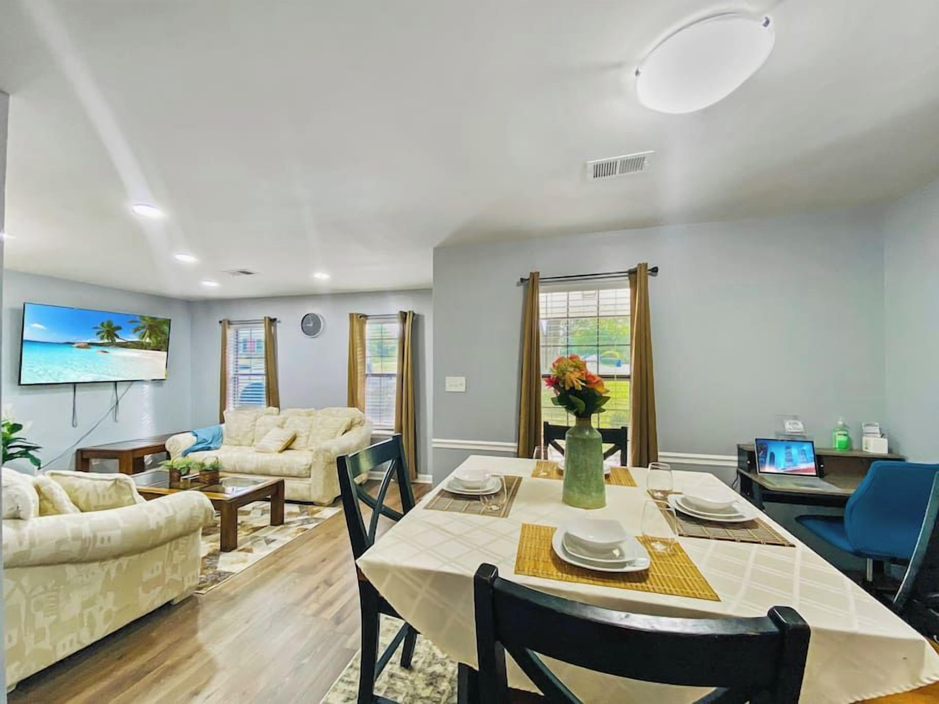 Ein Essbereich mit einem Tisch für vier Personen, einer Sofagarnitur und einem an der Wand montierten Fernseher.