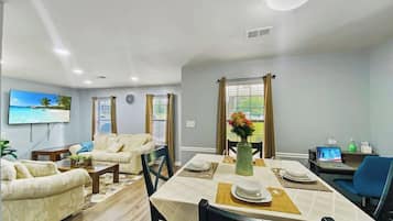 A dining area with a table set for four, a sofa set, and a television mounted on the wall.