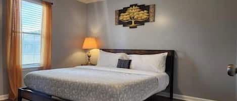 A bedroom with a bed, a nightstand, a lamp, a ceiling fan, and a wall-mounted artwork.