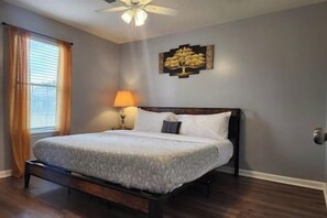 A bedroom with a bed, a nightstand, a lamp, a ceiling fan, and a wall-mounted artwork.