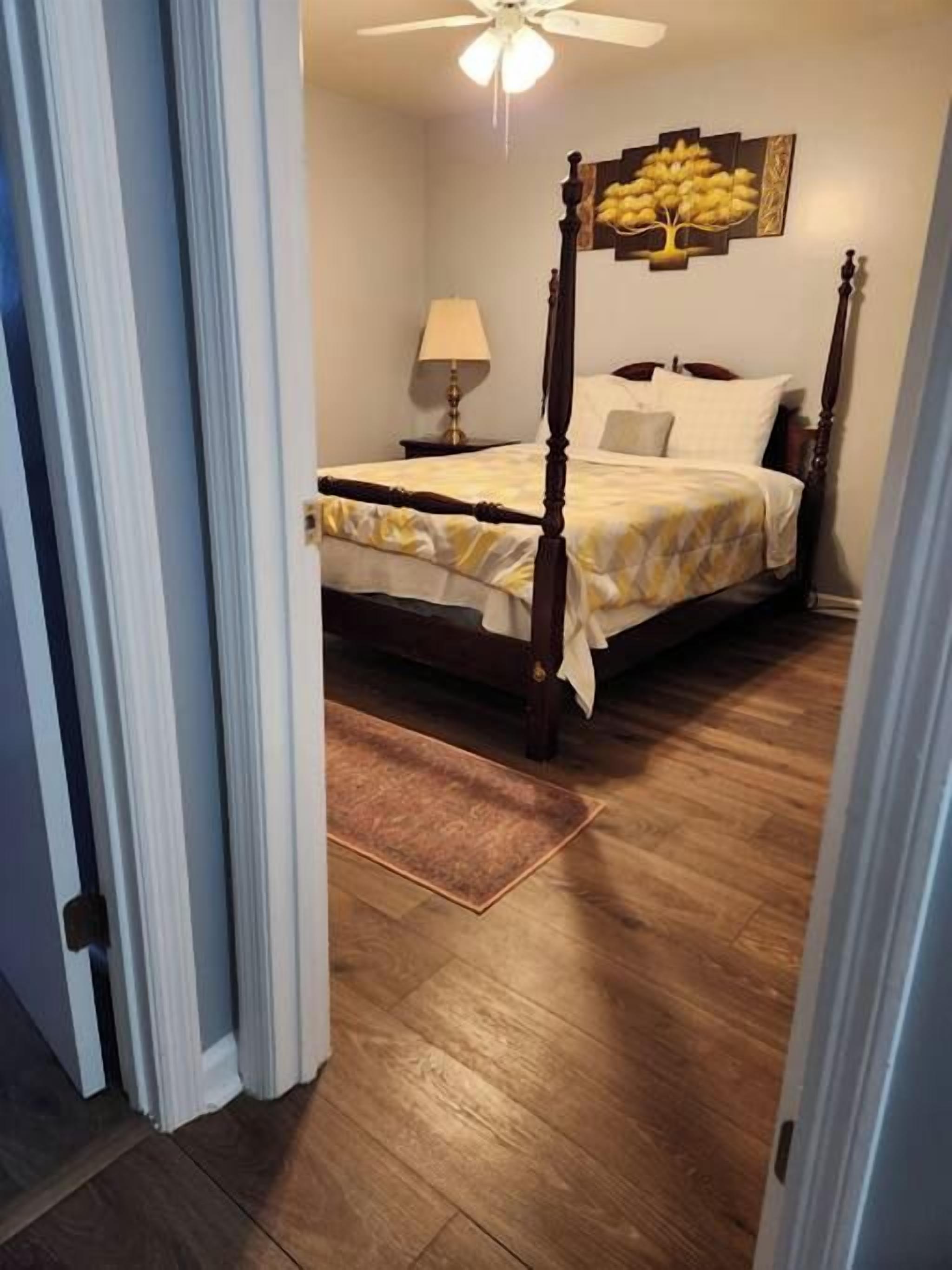 A bedroom with a four-poster bed, a nightstand, a lamp, and a ceiling fan.