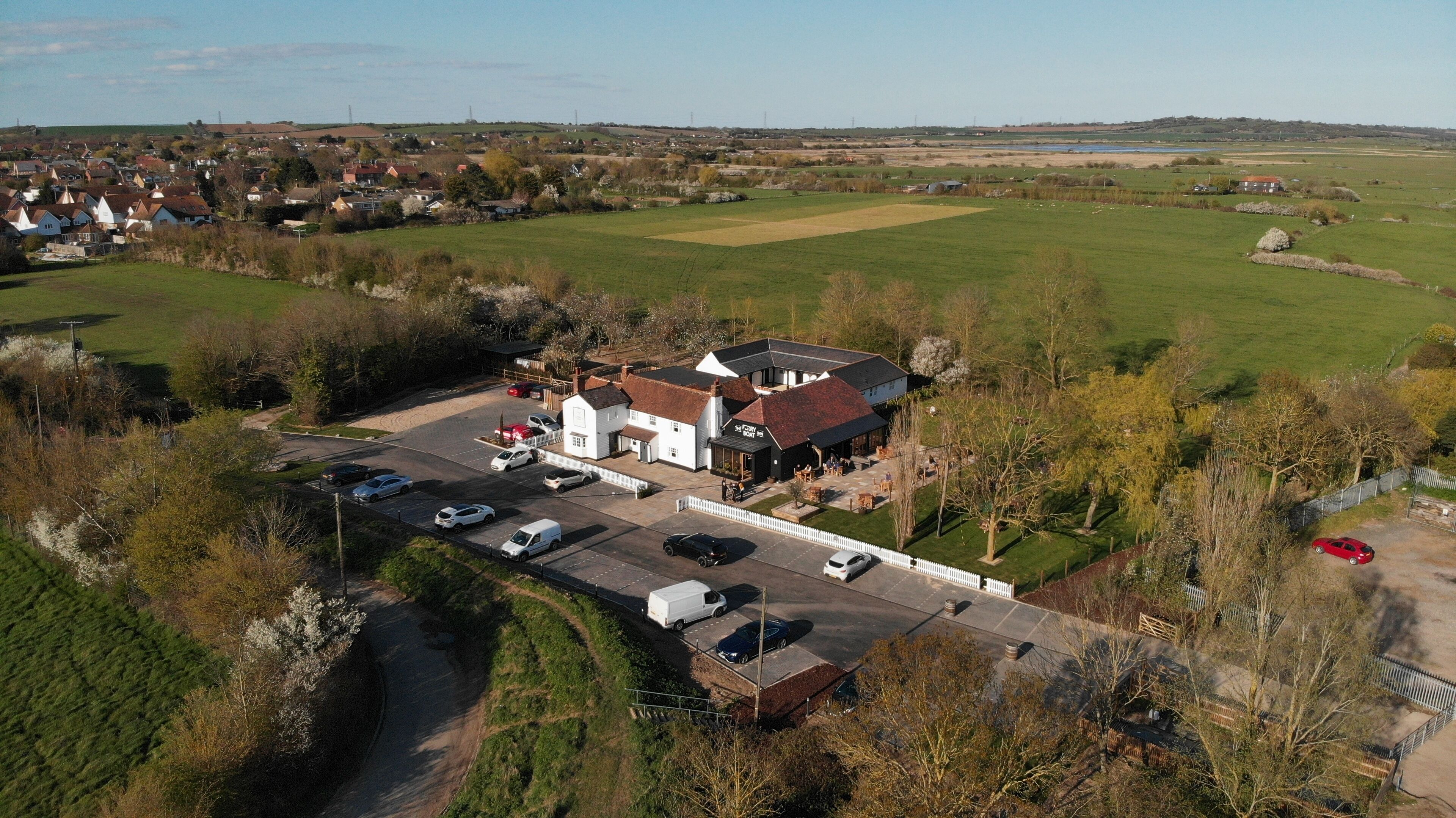 An aerial view of a rural hotel with a parking lot, a small garden, and a view of the surrounding countryside.
